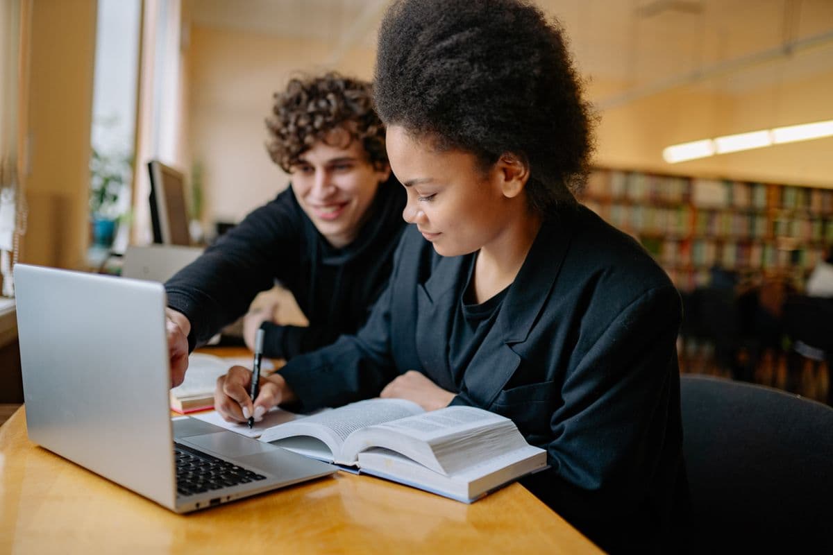 Duas pessoas consultam materiais de estudo em uma biblioteca.